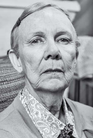 Serious elderly lady in sweater looking down at cameraの写真素材