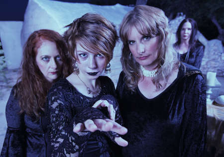 Three pretty witches in black standing outdoors near templeの写真素材