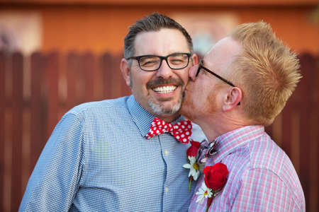 Smiling man with eyeglasses being kissed by spouseの写真素材