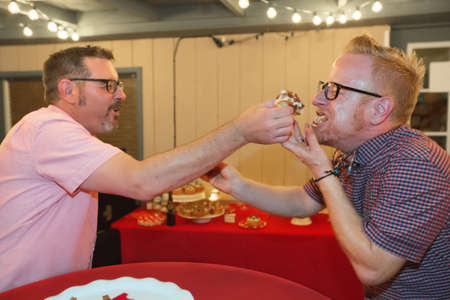 Gay male couple share bacon cupcake at their weddingの写真素材