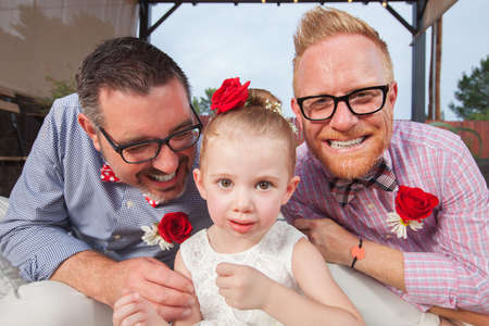 Smiling gay couple with daughter sitting outdoorsの写真素材