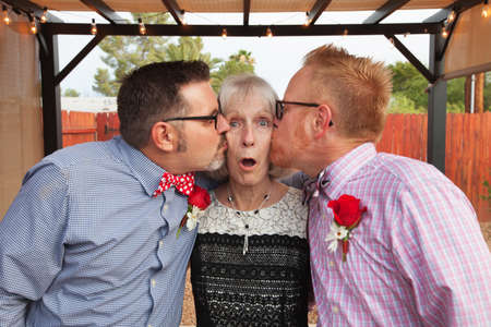 Blushing senior woman kissed by two handsome menの写真素材