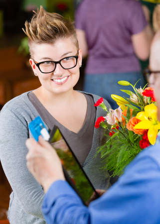 Female customer in a busy flower shop paying with creditの写真素材