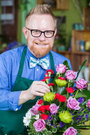 Dapper man wearing eyeglasses and apron creating a flower arrangementの写真素材