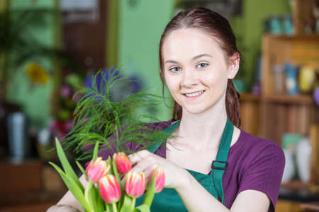 Beautiful young woman in green apron creating a tulip arrangementの写真素材