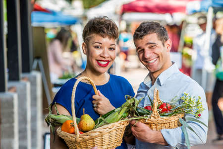 Smiling couple with baskets of produce at farmers marketの写真素材