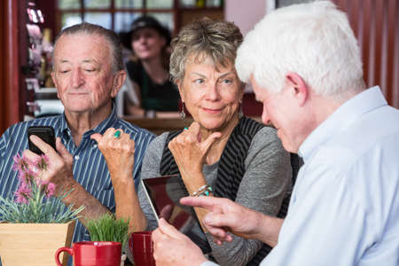 Mature woman in a coffee house gestures towards men distracted by their devicesの写真素材