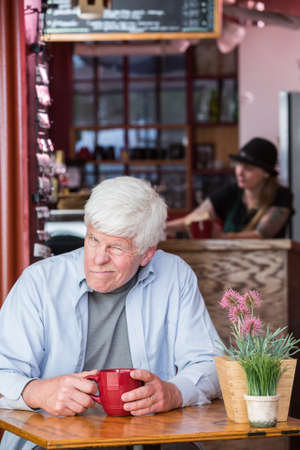 Grumpy mature man sitting by himself in a coffee houseの写真素材