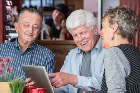 Happy mature friends on wifi with tablet computer in a coffeehouseの写真素材