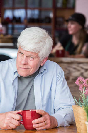 Grumpy mature man in a coffee house hunched over at tableの写真素材