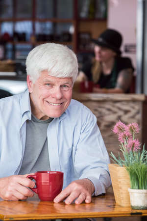 Happy mature man sitting alone at table in a coffee houseの写真素材