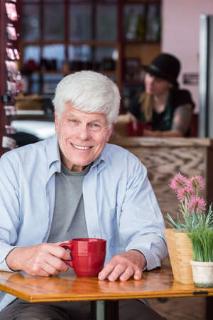 Happy senior citizen man in a coffee house with red mugの写真素材