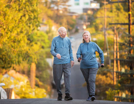 Enthusiastic man and woman with dumbbell weights walking up hill on streetの写真素材