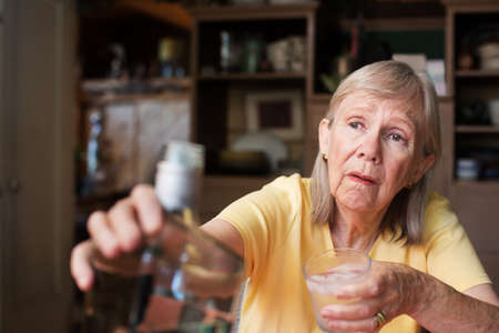 Lonely senior adult female reaching for a bottle of liquor while holding a glass