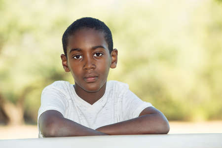 Serious African child seated at table with folded armsの写真素材