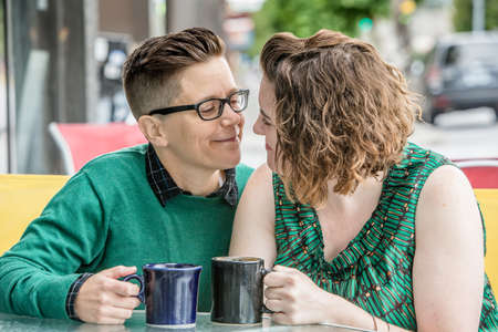 Romantic lesbian couple at bistro outdoors with coffee mugs in handの写真素材