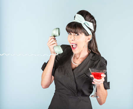 Excited retro woman in black dress with cosmopolitan cocktail and phone receiver
の写真素材