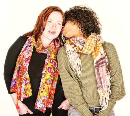 African American woman whispering into ear of friend wearing scarfの写真素材