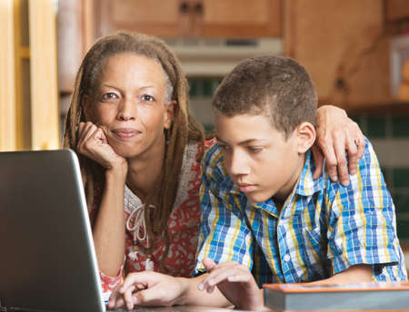 African-American mother supervises her teenaged son as he studies on his computerの写真素材
