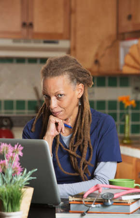One female medical student studying in her kitchen on laptop with books and stethoscopeの写真素材