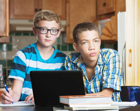 Pair of serious teen friends in kitchen with school textbooks and laptopの写真素材