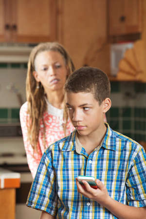 Teenaged son holds cell phone as his curious mother looks questioninglyの写真素材