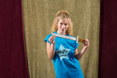 Young female actress holds dagger in both hands and stares at cameraの写真素材