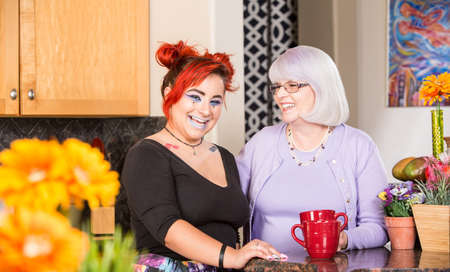 Mother and daughter stand in kitchen laughingの写真素材