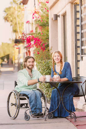 Woman and male friend in wheelchair having coffeeの写真素材