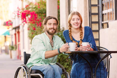 Woman having coffee with male friend in wheelchair at outdoor cafeの写真素材