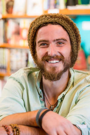 Smiling young man with knit cap in book store or libraryの写真素材