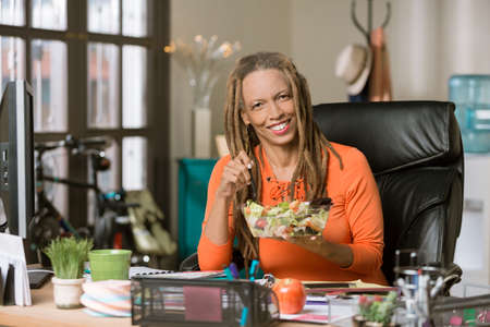 Stylish professional woman with dreadlocks having a healthy lunch in her officeの写真素材