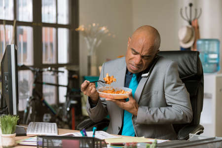 Professional man working through lunch eating packaged foodの写真素材