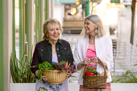 Two senior women returning with baskets of produce from farmers marketの写真素材
