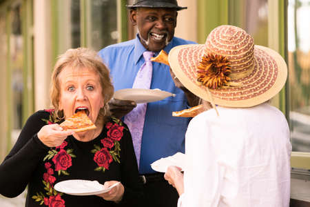 Three seniors eating slices of pizza downtownの写真素材