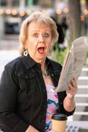 Woman downtown with newspaper reacting to storyの写真素材