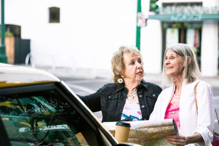 Two women in a city center holding road mapの写真素材