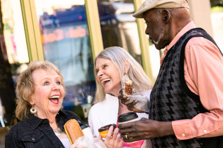 Three seniors downtown eating donuts and laughingの写真素材