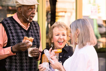 Three seniors eating donuts and laughingの写真素材