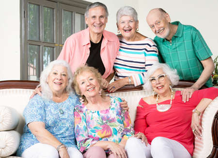 Six cheerful senior friends around an antique couchの写真素材