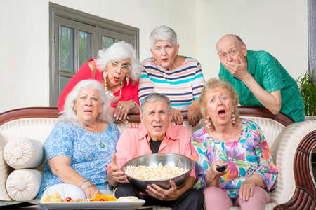 Six unhappy senior friends reacting to televisionの写真素材