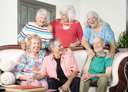 Six senior friends laughing around an antique couchの写真素材