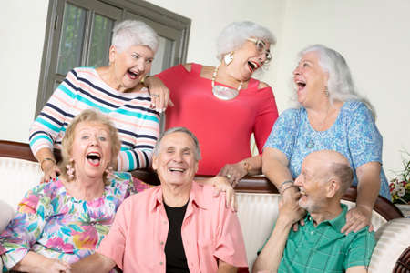 Six amused senior friends laughing out loud around an antique couchの写真素材