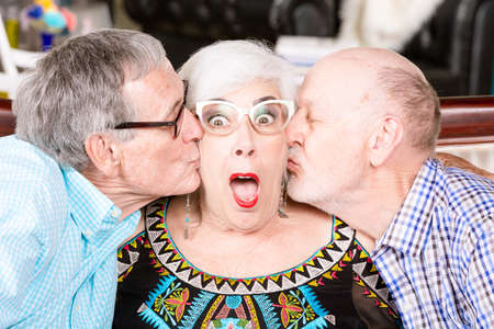 Two senior men kissing the same womanの写真素材