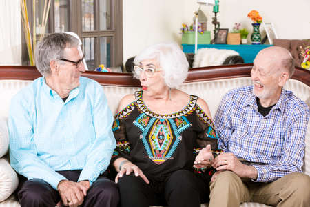 Two senior men with woman on a living room couchの写真素材