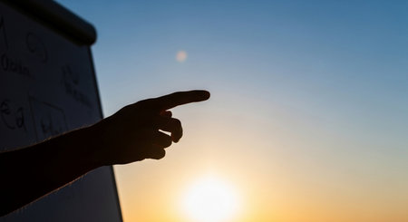 Male hand pointing at a whiteboard against the background of the setting sunの素材