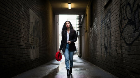 Portrait of a beautiful brunette girl in a black jacket with a red hat in a dark alleyの素材