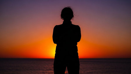 Silhouette of a young woman at sunset on the beach.の素材