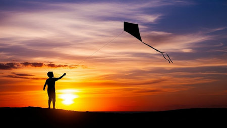 Silhouette of a woman flying a kite at sunset.の素材