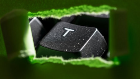 Keyboard 'T' Key Visible Through a Torn Green Paper Hole, Hinting at Typingの素材